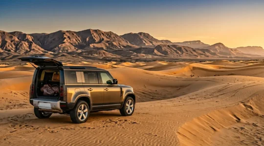 Vue panoramique d'un élégant 4x4 garé sur une dune dorée au premier plan avec des clubs de golf visibles, les montagnes de l'Atlas en arrière-plan