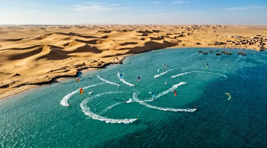 Vue aérienne d'une lagune turquoise avec kitesurfers naviguant entre désert et océan