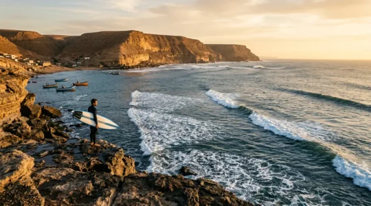 Surfeur contemplant les vagues depuis les falaises rocheuses de Taghazout avec vue panoramique sur la baie